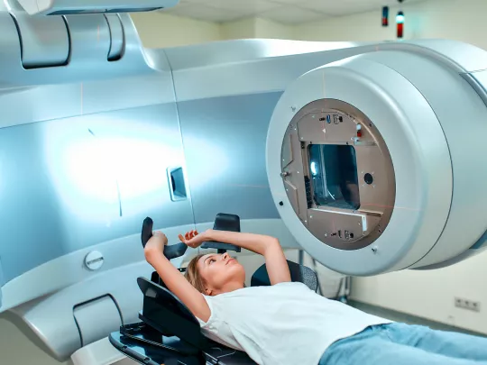 한 여성이 방사선 치료기 앞에 있는 의료용 소파에 누워 있습니다.