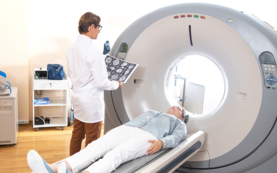 MRI 장비 옆에 뇌 스캔을 들고 있는 의사와 누워 있는 환자.